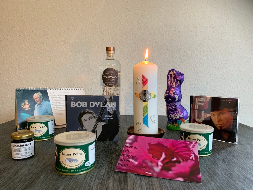 Gabentisch mit Milka-Osterhase, Gin aus der Region, Wurst und Holundergelee vom Lieblingshofladen, CDs von Bob Dylan und Garth Brooks, ein Ostergruß und die brennende Osterkerze