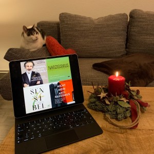 Dunkelrote, fast verblühte Amaryllis auf meinem Wohnzimmertisch, daneben, farblich passend, eine brennende Kerze, dahinter die Couch und davor mein iPad mini mit den Miniatouransichten der vier Hörbücher.