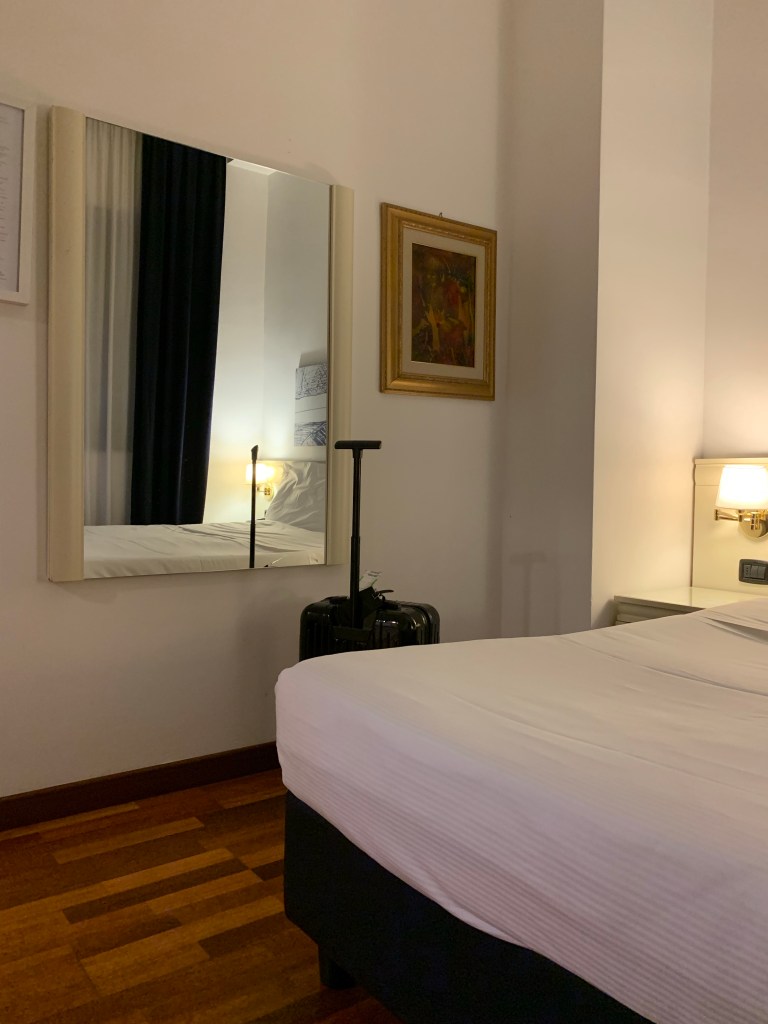 Hotelzimmer mit Spiegel, Nachttischlicht und meinem Rollkoffer.