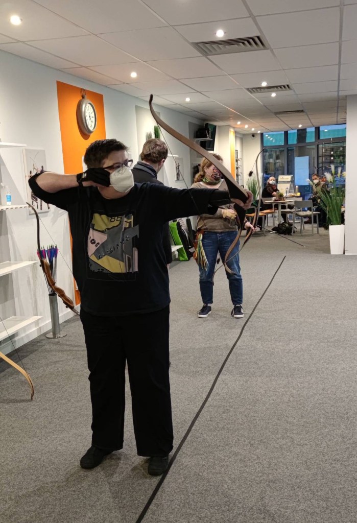 Ich mit Maske beim Schießen mit stark gekipptem Bogen, indoor.