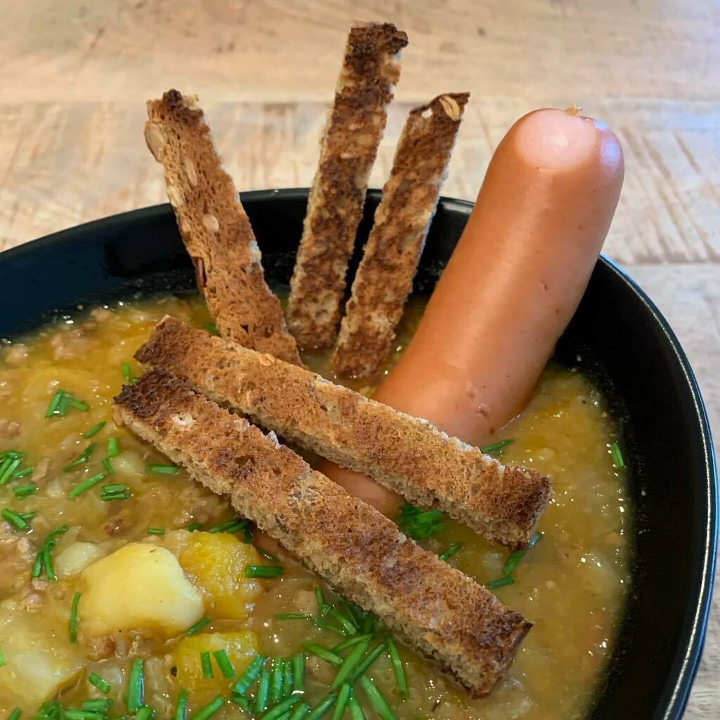Herbsteintopf, angerichtet mit einem dicken Bockwürstchen, gerösteten Brotstreifen und mit Schnittlauch überstreut.