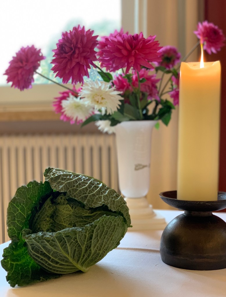 Ein kleiner Kopf Wirsing neben Altarblumen und brennender Altarkerze.