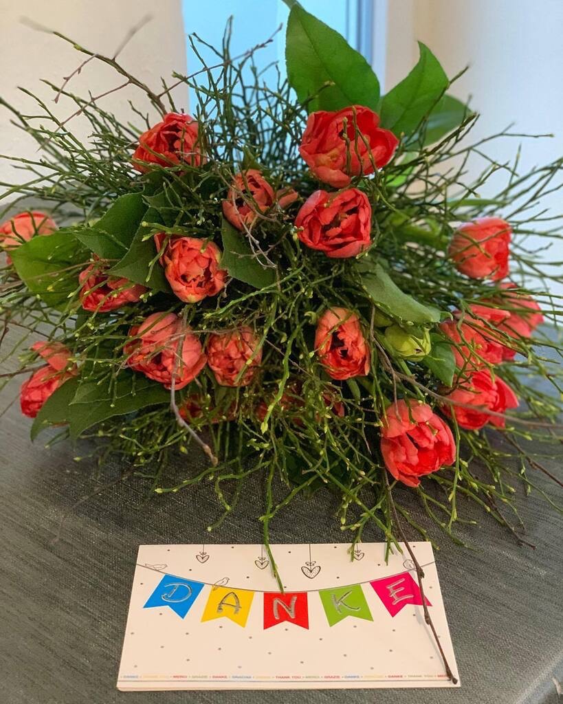 Großer Blumenstrauß mit roten Tulpen und viel Grün, davor eine Klappkarte, auf der in großen Lettern "Danke" steht.