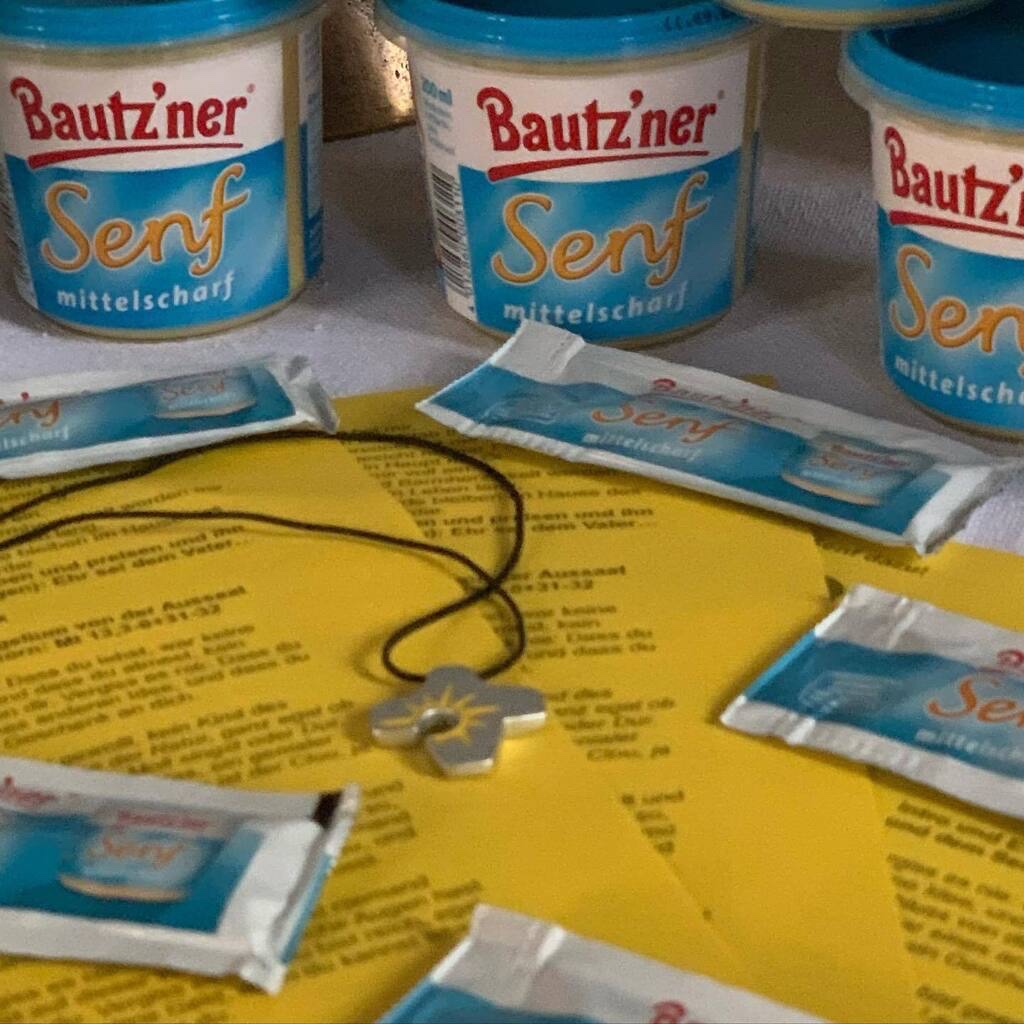 Einige Senftöpfe und -tütchen, Liedblätter und Umhängekettchen wie im Text beschrieben fürs Foto dekorativ zurechtgelegt.