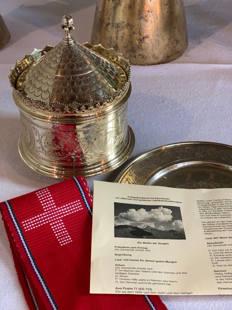 Pyxis und Patene (Hostiendose und -teller), rote Stola und Liedblatt auf den Altar.