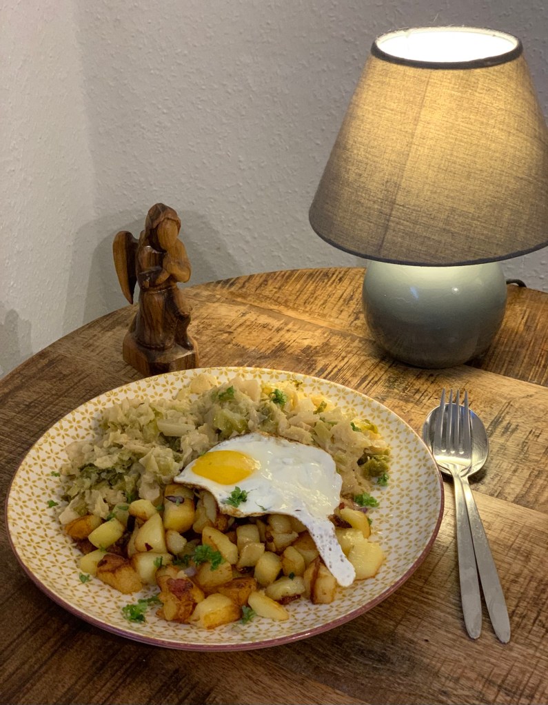 Das beschriebene Mittagessen auf einem Teller, umgeben von einem knienden Olivenholzengel , einer Tischlampe, Gabel und Löffel.