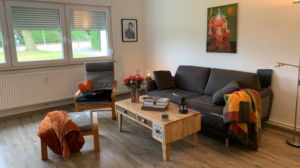 Die Sitzeckenseite meines Wohnzimmers. Man sieht die neue Couch und den sauberen Pöng nebst Hocker, wo hier und da die Kratzschutzfolie schimmert. Dazu die neuen Wolldecken und auf dem Pöng das Katzennest.