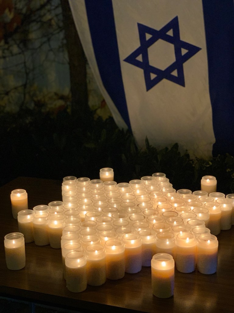 Der Davidstern aus Kerzen gestellt, dahinter die Flagge Israels.