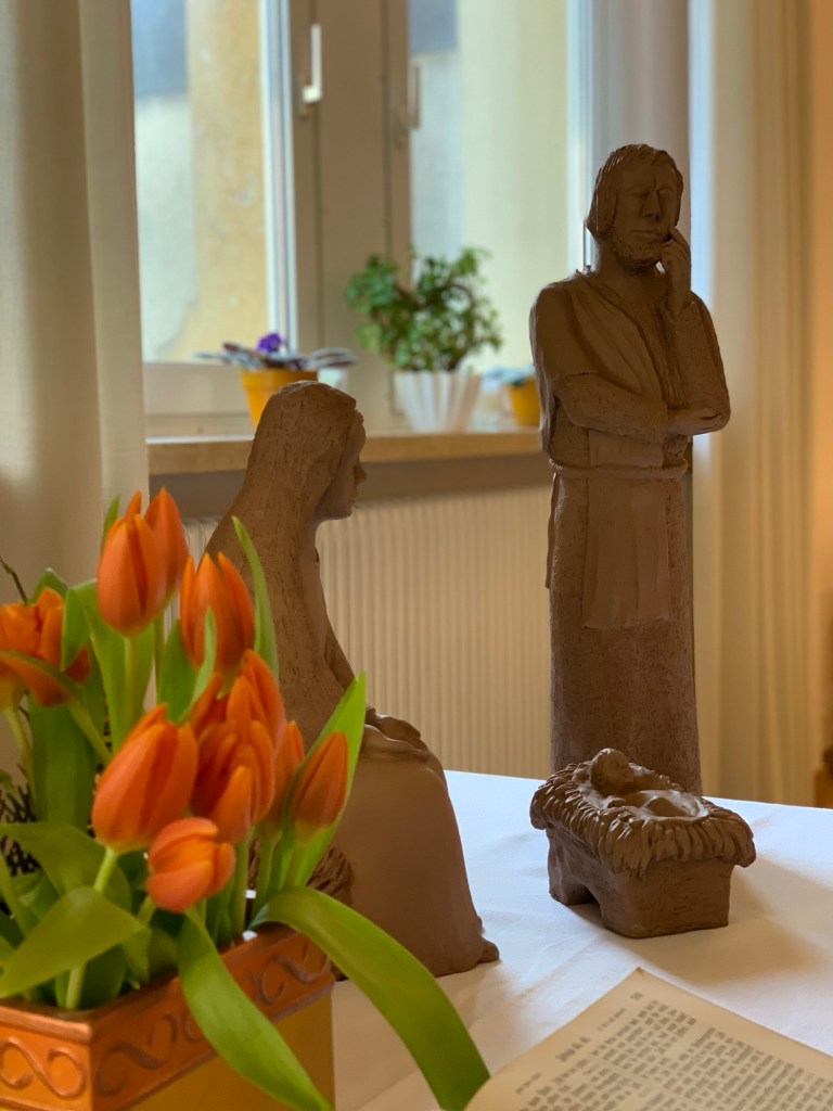Tulpen und die Bibel auf dem Altar. Rechts davon Maria, Josef und das Kind in der Krippe als Tonfiguren.