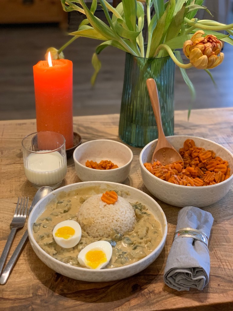 Das Essen wie beschrieben und hübsch angerichtet mit der Schwerpunktfarbe Orange: Orangene Tulpen, eine orangene Kerze, Möhrensalat in großer und kleiner Schüssel, ein Möhrenscheibchen auf der Reiskugel. Daneben das Ei ins zwei Hälften mit dem orangenen Dotter.