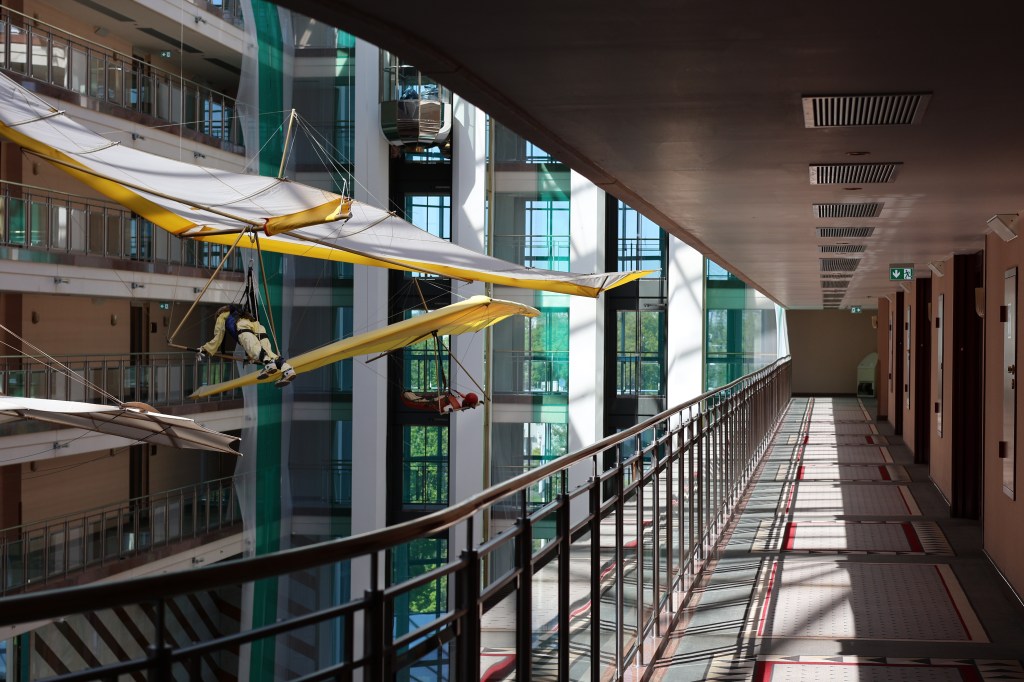 Mein Hotelflur, der aber nach links offen ist, weil er in Ballustraden um eine riesige Hotelhalle führt. Dort schweben große Puppen als Drachenflieger und mit historischen Flugversuchsflügeln.