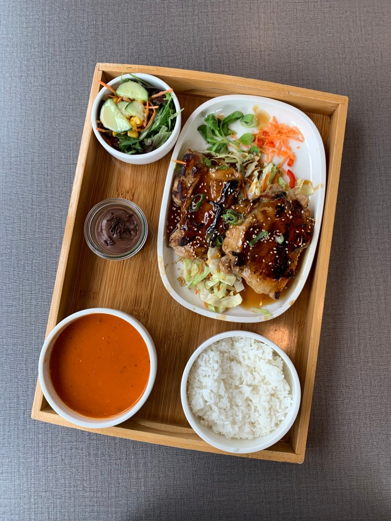 Mittagessen auf einem Tablett wie beschrieben: Hühnchen auf einem Teller, alles Weitere in Schälchen drumherum.